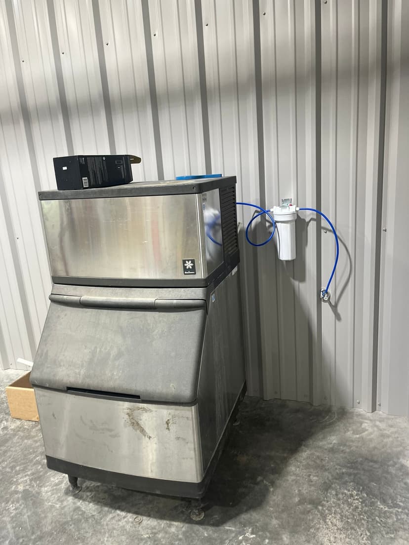 Commercial ice machine against a metal wall with water filtration system connected.